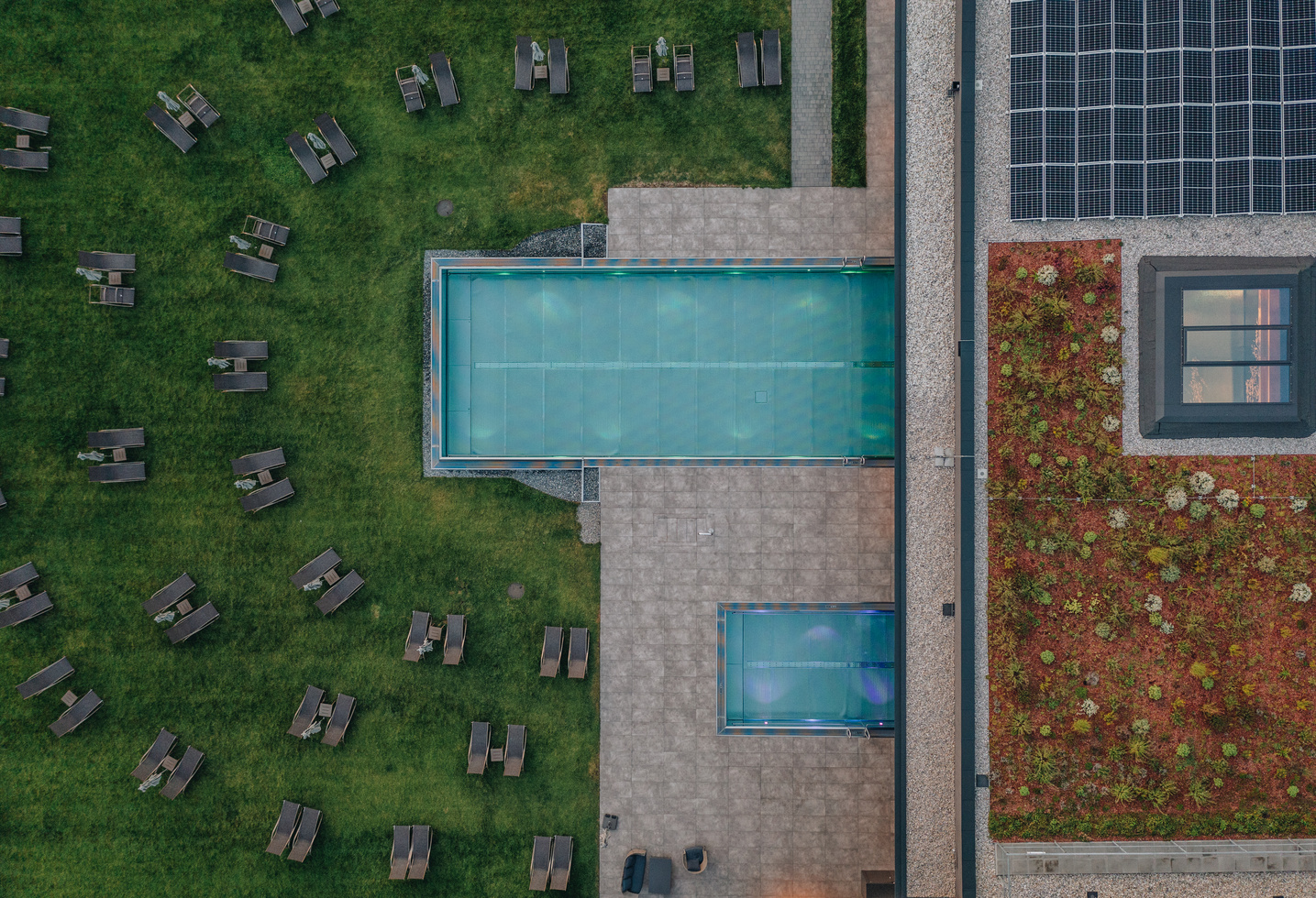 Luftaufnahme eines Pools auf dem Dach, einer Terrasse und einer grünen Wiese mit verstreuten Liegestühlen.
