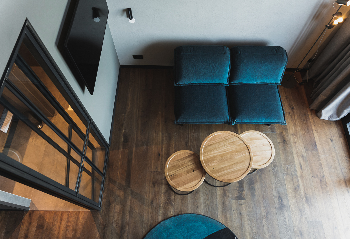 Modern living room with blue seating furniture, round wooden tables and wooden floors, seen from above.