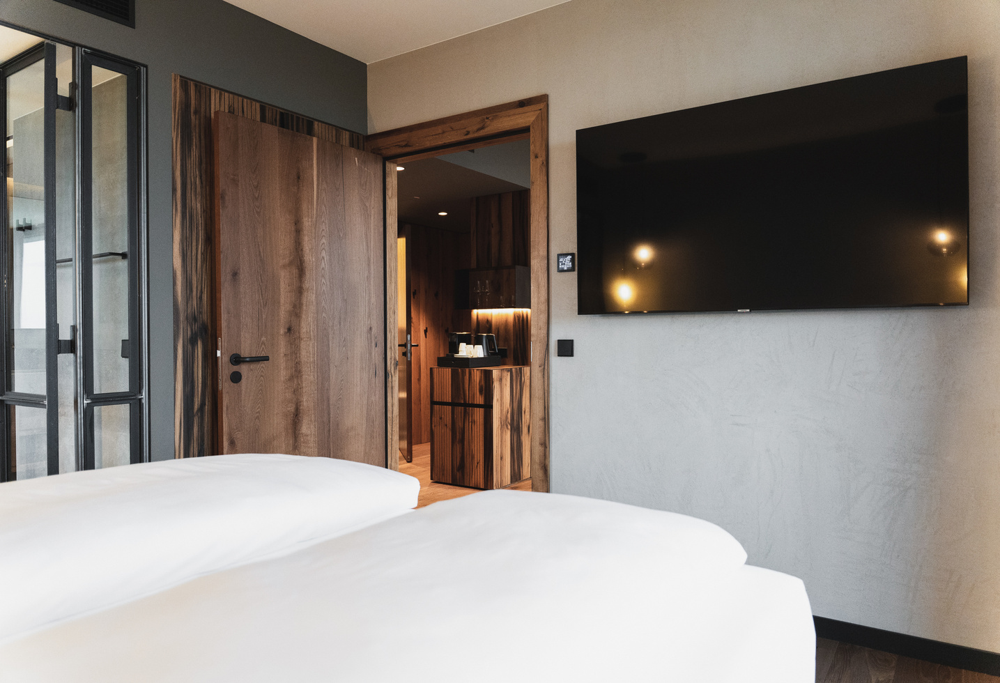 A modern hotel room with a large TV, a wooden door and neatly made single beds in the front.