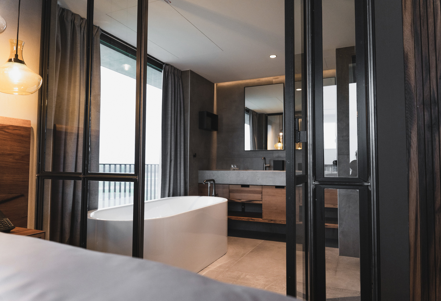 Modern bathroom with free-standing bathtub, large mirror and glass partitions, seen from one bedroom.