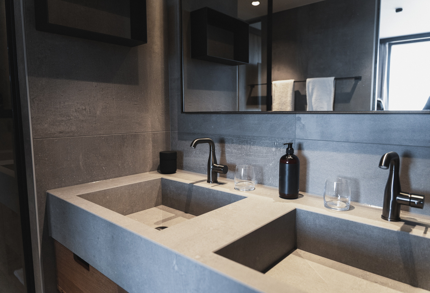 Modernes Badezimmer mit Doppelwaschbecken, schwarzen Armaturen, Spiegel und Toilettenartikeln auf einer grauen Arbeitsplatte.