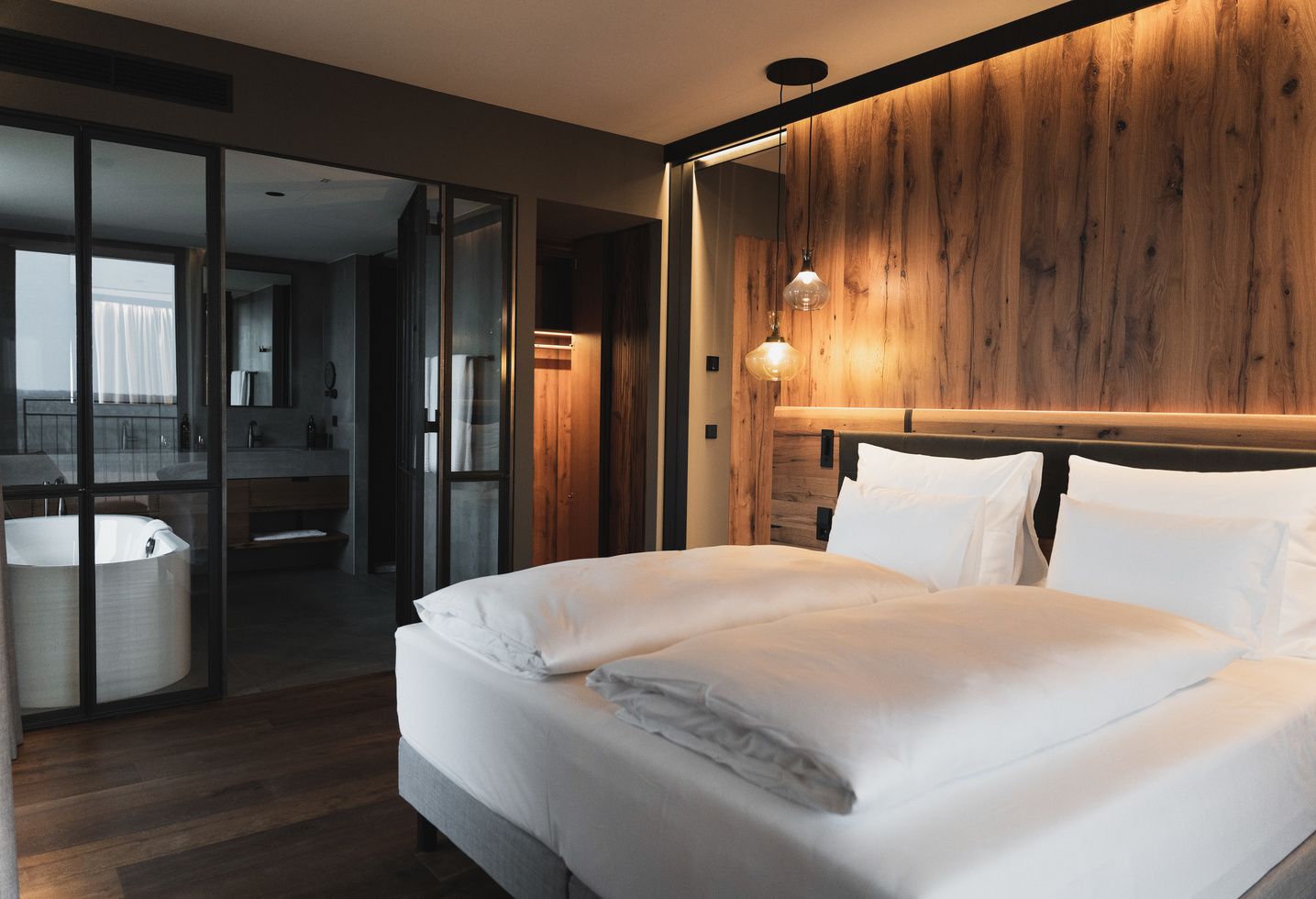Modern hotel room with a large bed, a wooden wall and an open bathroom with bathtub.