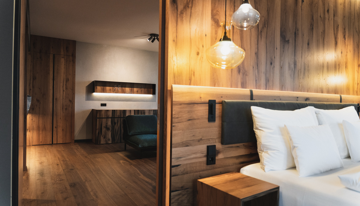 Modern hotel room with wood-paneled walls, a bed with white pillows and hanging pendant lights.