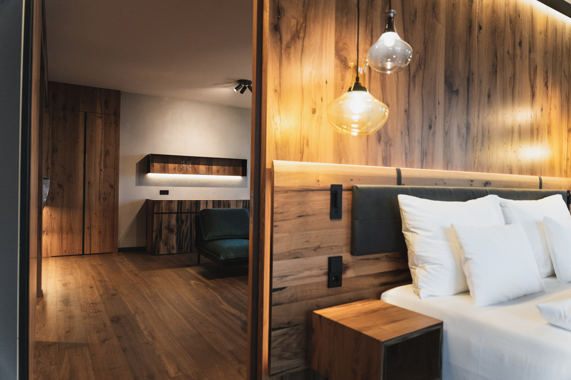 Modern hotel room with wood-paneled walls, a bed with white pillows and hanging pendant lights.