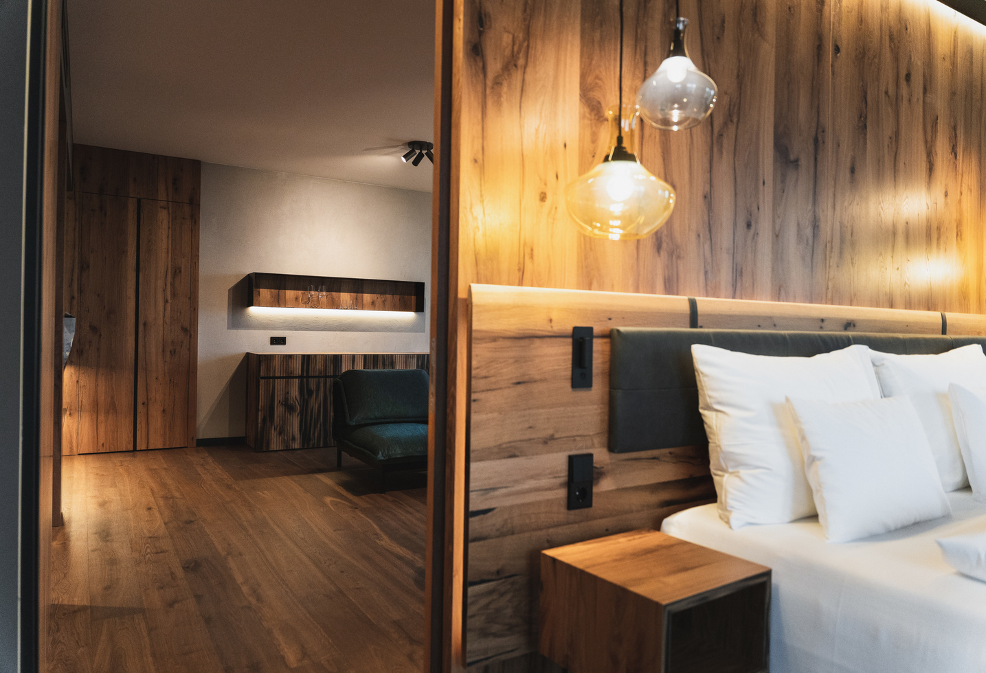 Modern hotel room with wood-paneled walls, a bed with white pillows and hanging pendant lights.
