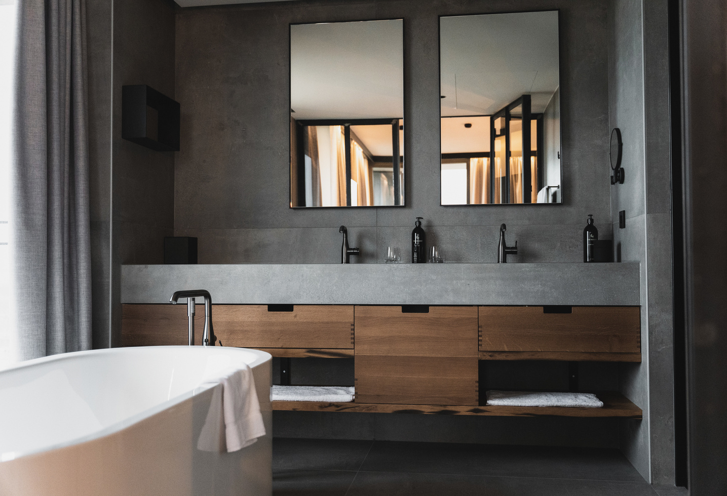 Modern bathroom with double washbasin, large mirrors, a white bathtub and wooden cabinets.