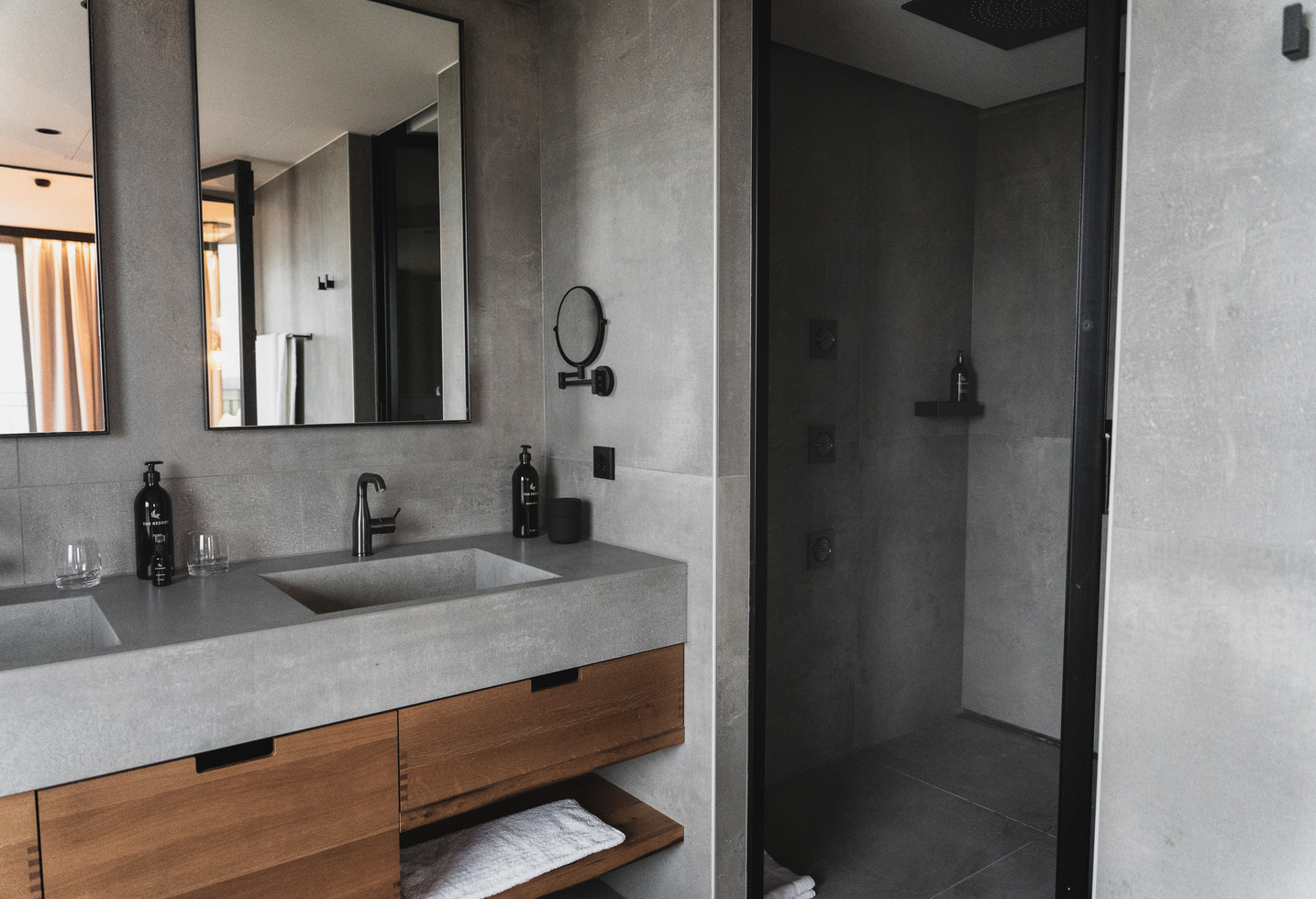 Modern bathroom with gray walls, double sinks, large mirrors and an open shower area with black fittings.