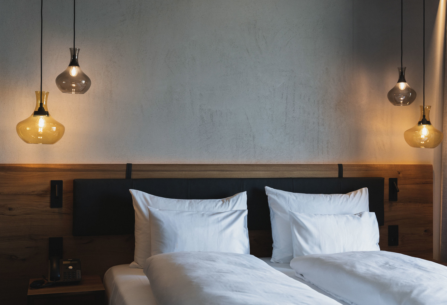 Modern hotel room bed with white bed linen and pillows, wooden headboard and hanging lamps.