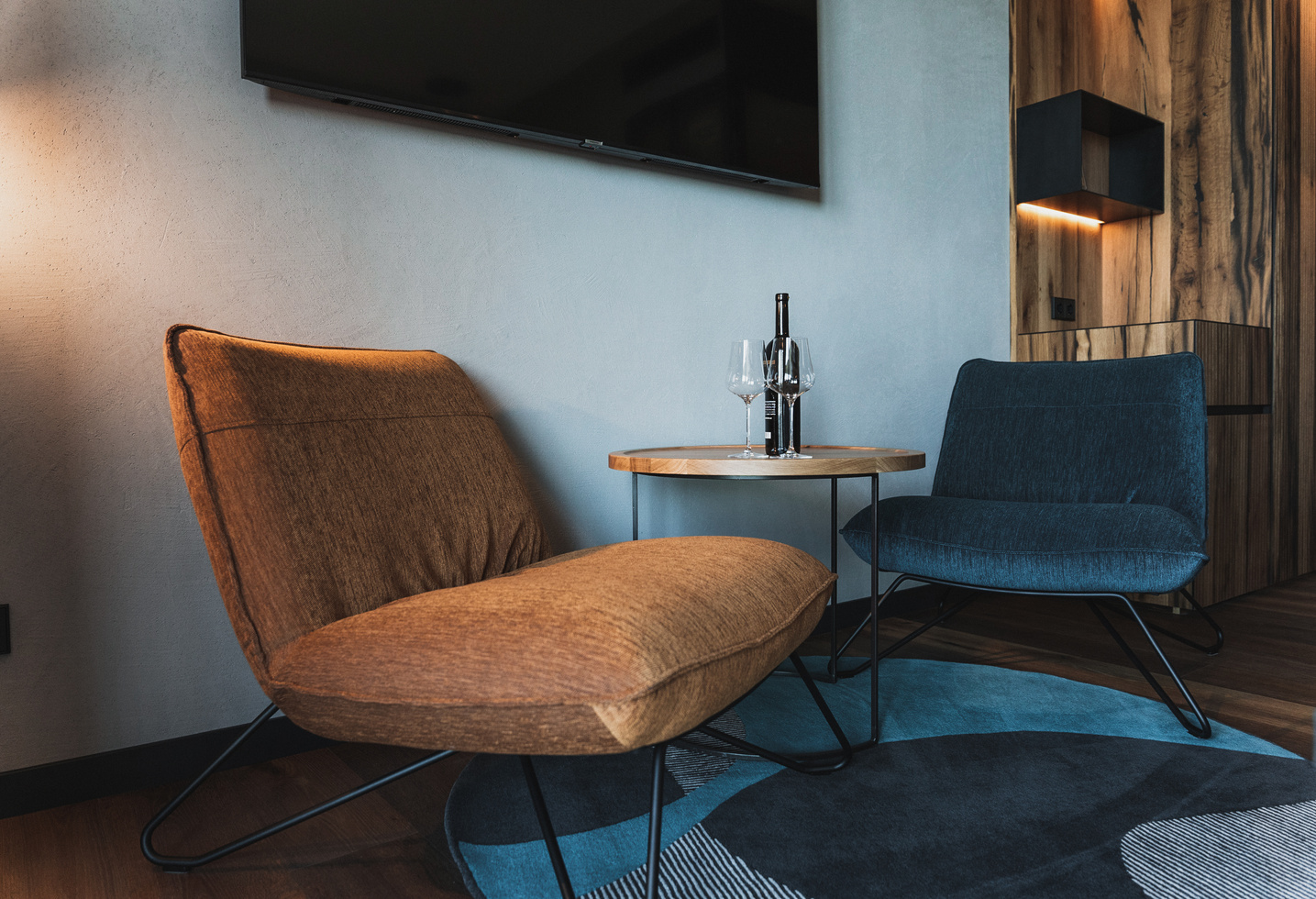 Two modern lounge chairs and a small round table with wine and glasses in a stylish, cozy room.