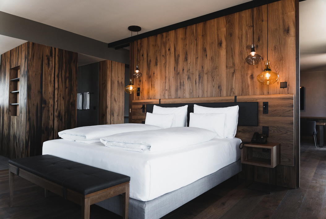 Modernes Hotelzimmer mit großem Bett, weißer Bettwäsche, holzvertäfelten Wänden und Hängelampen.