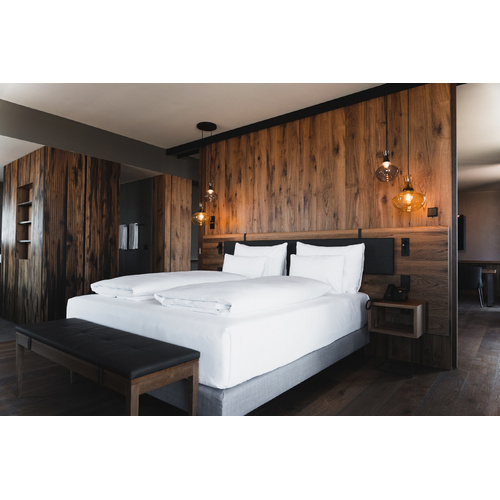 Modernes Hotelzimmer mit großem Bett, weißer Bettwäsche, holzvertäfelten Wänden und Hängelampen.