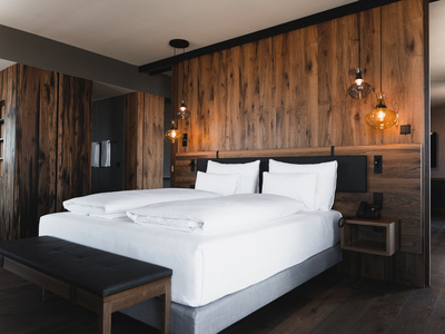 Modernes Hotelzimmer mit großem Bett, weißer Bettwäsche, holzvertäfelten Wänden und Hängelampen.