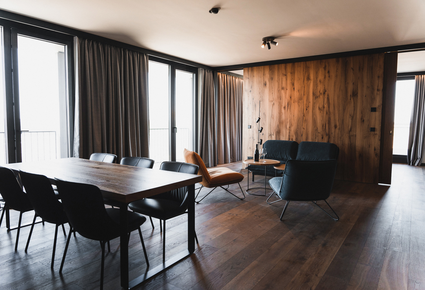 Modern living and dining area with wooden floors, large windows and minimalist furniture.