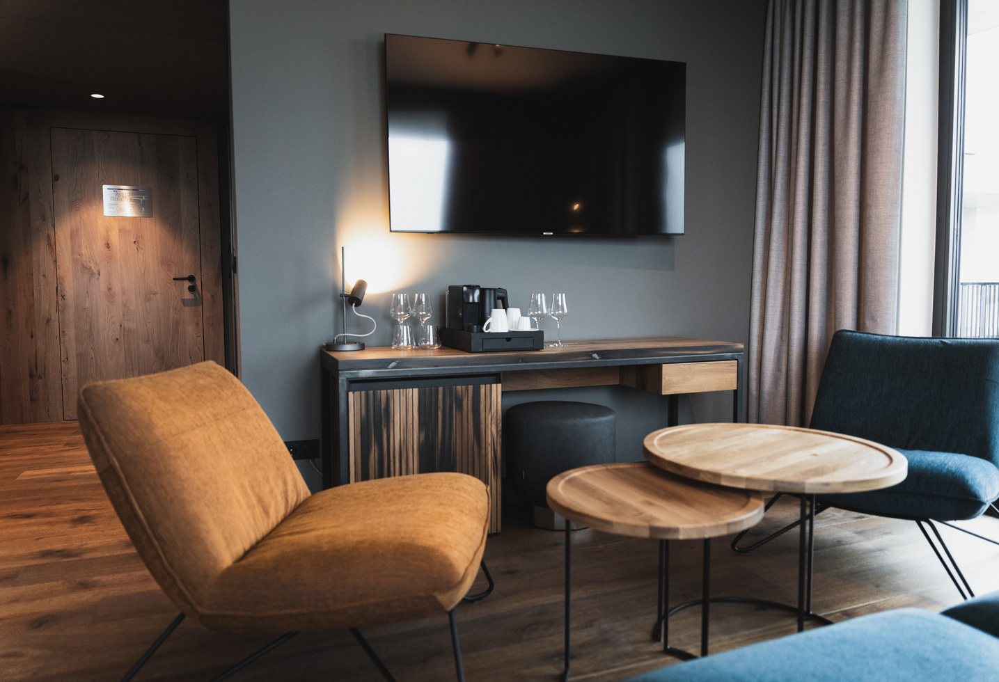 Modernes Hotelzimmer mit TV, Kaffeemaschine, runden Tischen und gemütlichen Stühlen in einem stilvollen, minimalistischen Ambiente.
