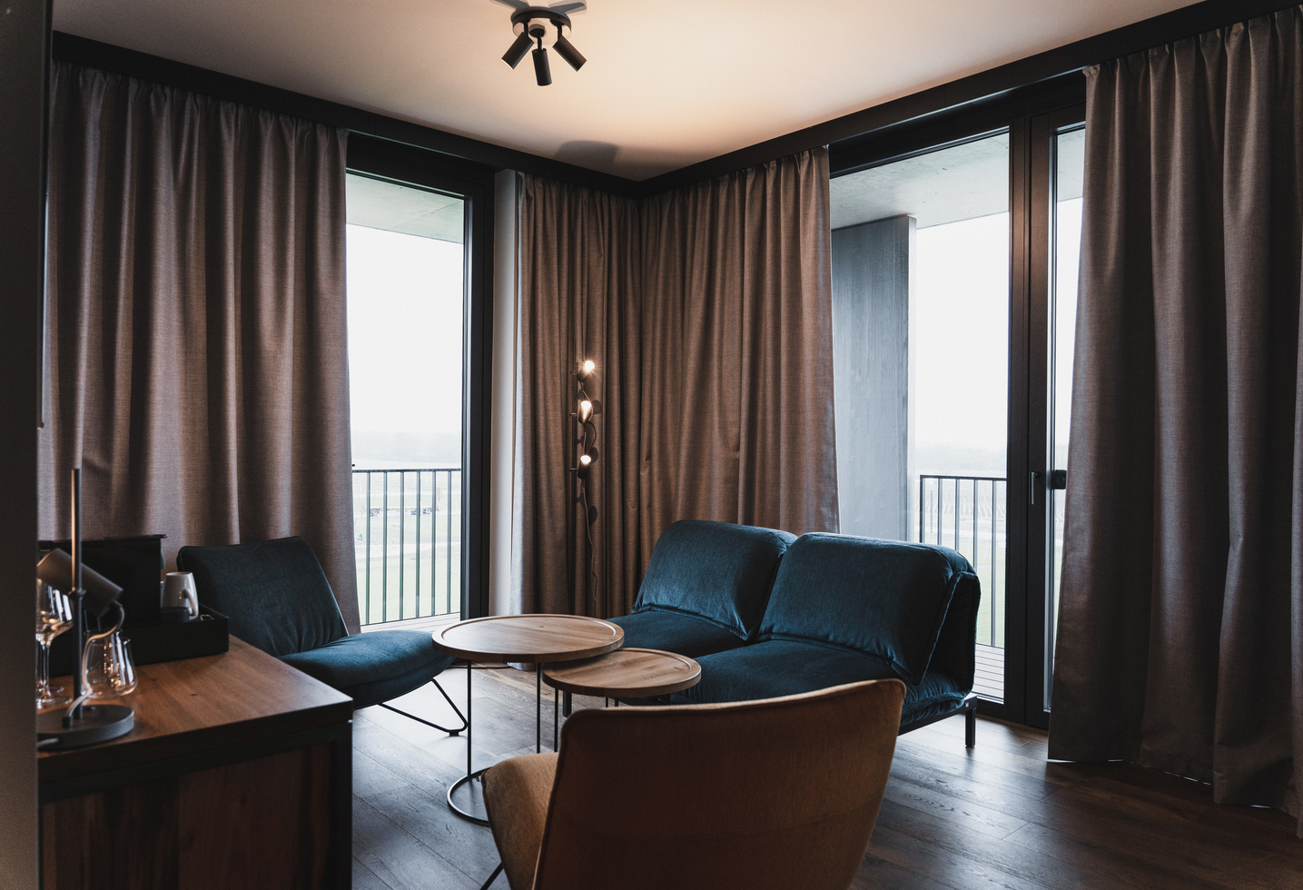 Modernes Wohnzimmer mit blauen Sofas, einem runden Couchtisch und großen Fenstern mit grauen Vorhängen.