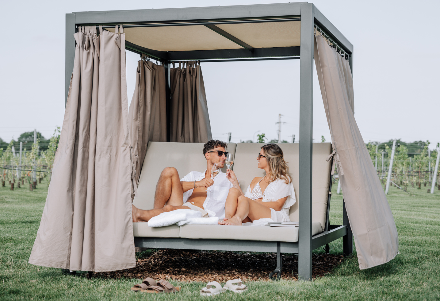 Ein Paar entspannt sich auf einer Cabana-Lounge im Freien, stößt mit Gläsern an und genießt einen sonnigen Tag.