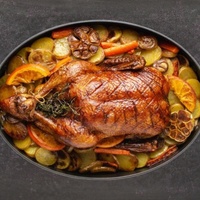 Hähnchen mit Kräutern, Kartoffeln, Karotten, Orangenscheiben und Knoblauch in einer schwarzen Bratpfanne braten.