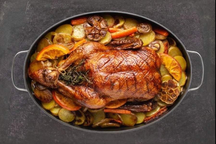 Hähnchen mit Kräutern, Kartoffeln, Karotten, Orangenscheiben und Knoblauch in einer schwarzen Bratpfanne braten.