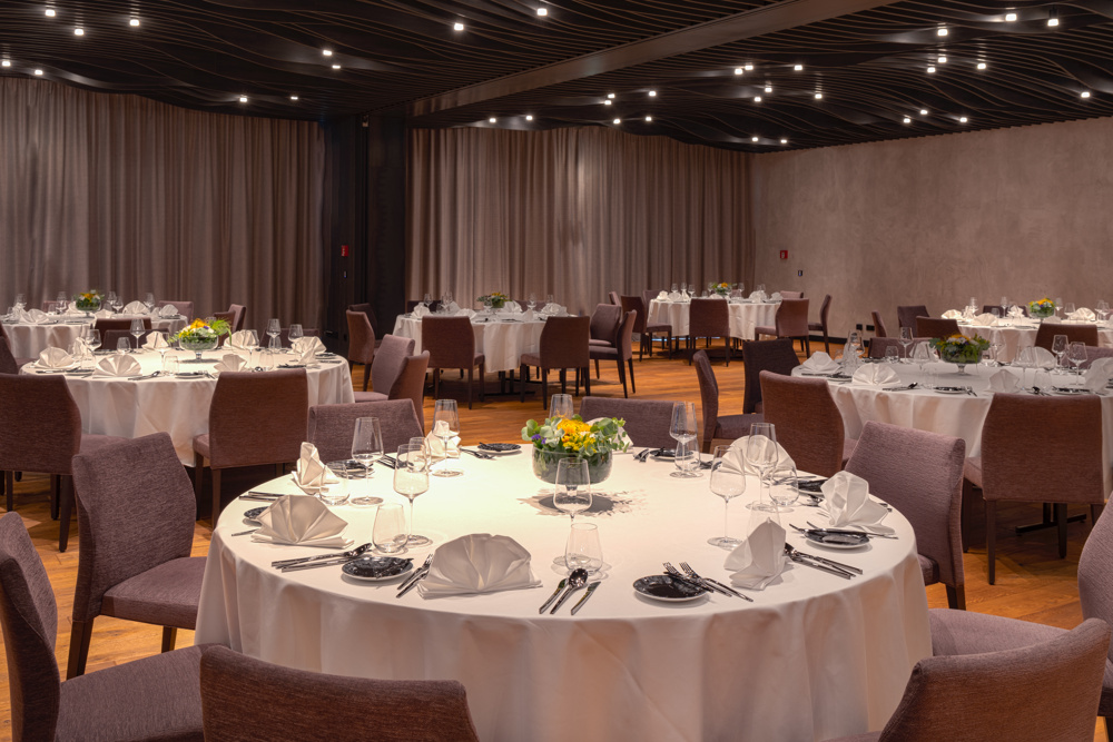 Eleganter Bankettsaal mit runden Tischen zum Essen, weißer Bettwäsche und Blumenschmuck.
