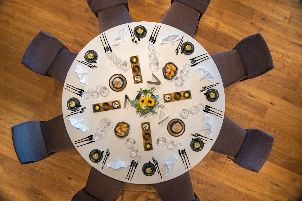 Ein runder, für acht Personen gedeckter Tisch mit Tellern, Gläsern, Servietten und einem Sonnenblumen-Mittelstück, von oben gesehen.