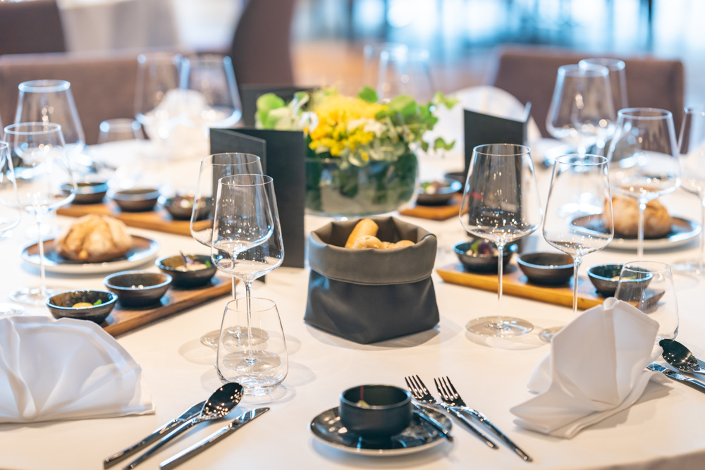 Elegant gedeckter Esstisch mit Gläsern, Tellern, Servietten und einem Blumen-Mittelstück in einem hellen Raum.