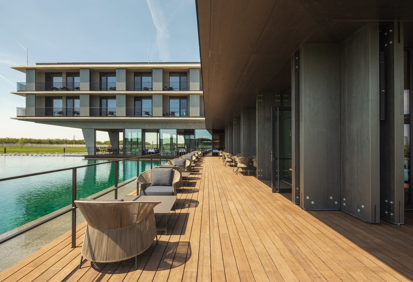 Modern hotel with a wooden terrace, outdoor seating and a reflecting pool under the open sky.