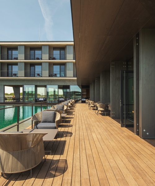 Modern hotel terrace with wooden decking, outdoor seating and views of the building and the water feature.