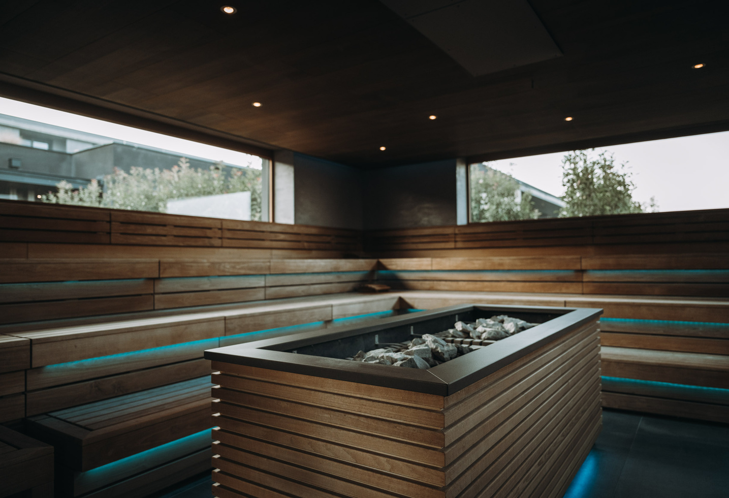 Moderne Holzsauna mit großen Sitzbänken und zentralem Steinofen, beleuchtet von sanften Lichtern.