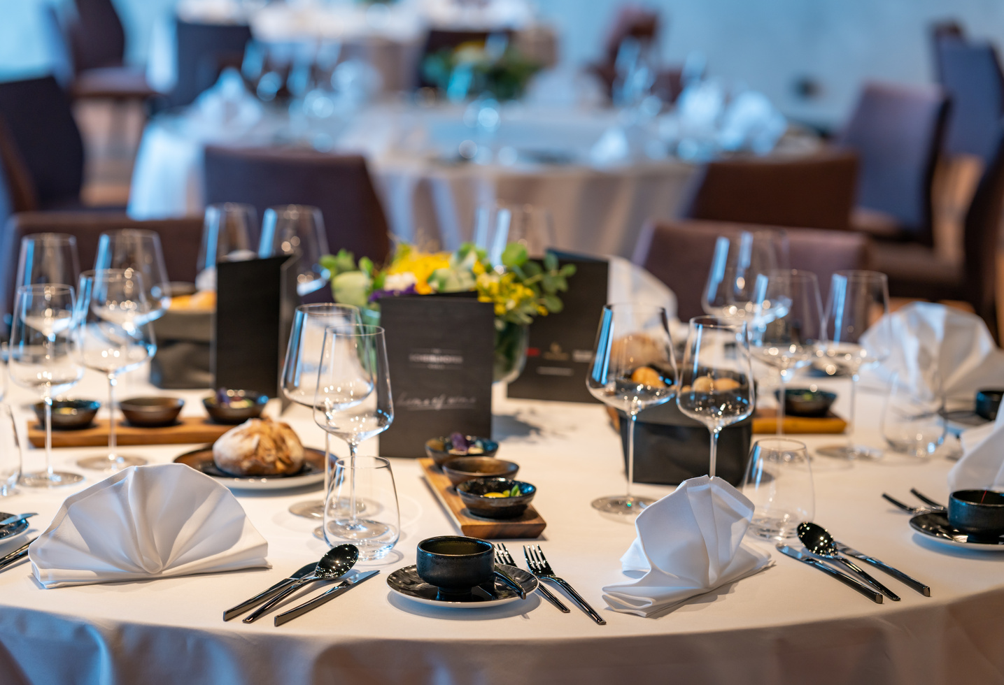 Ein runder Tisch für eine formelle Veranstaltung mit gefalteten Servietten, Gläsern, Tellern und einem blumigen Mittelstück.