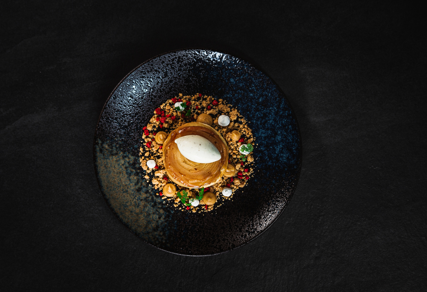 A gourmet dessert with ice cream, sprinkles and colorful toppings on a dark, elegant plate.