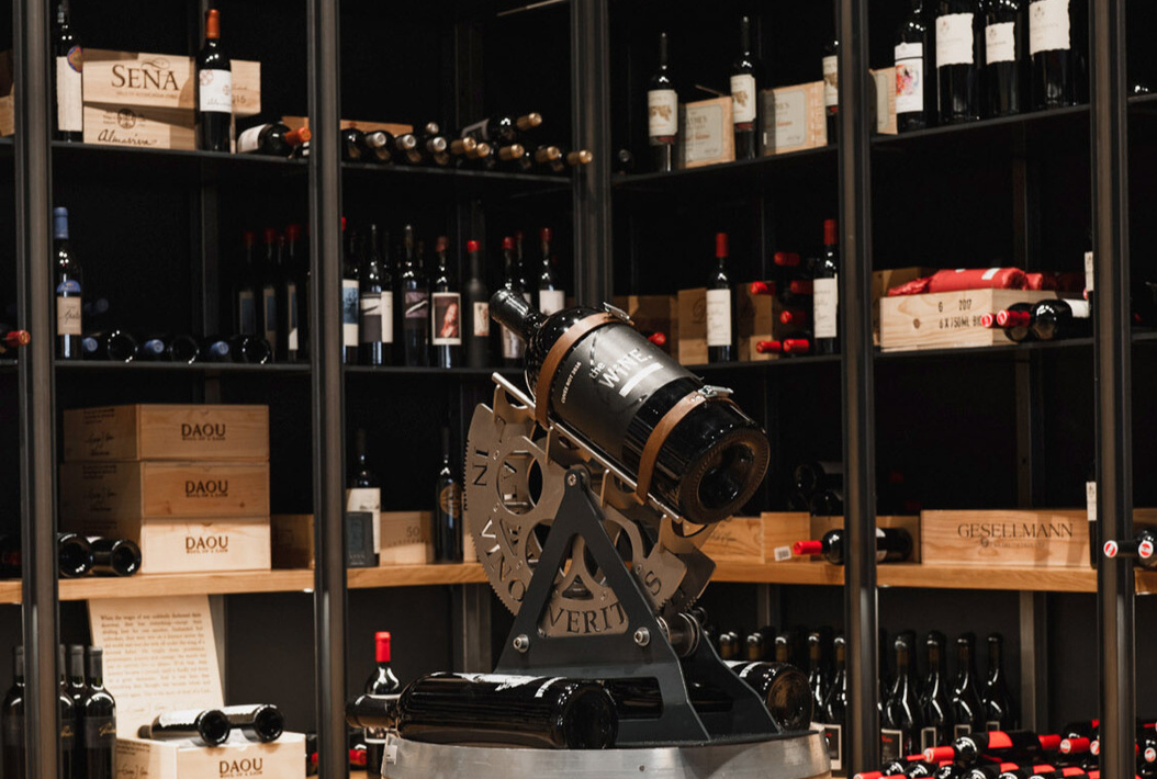 Large wine bottle on a metal stand in front of shelves filled with various wine bottles and wooden crates.