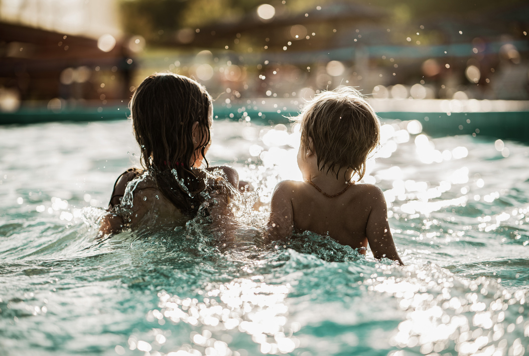 Zwei kleine Kinder spielen zusammen in einem sonnenbeschienenen Schwimmbecken, in dem das Wasser um sie herum plätschert.