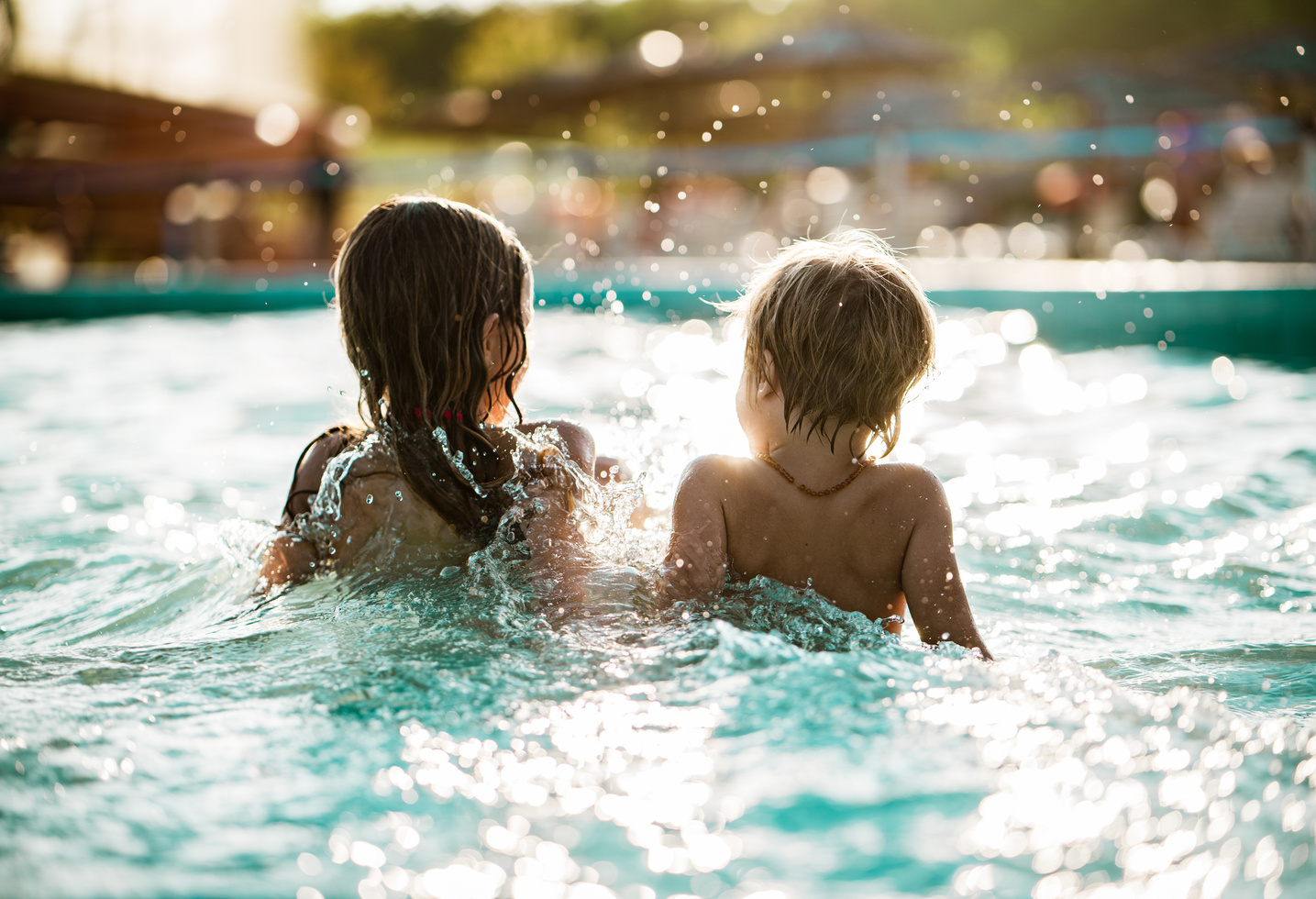 Zwei kleine Kinder spielen zusammen in einem sonnenbeschienenen Schwimmbecken, das Wasser plätschert um sie herum.