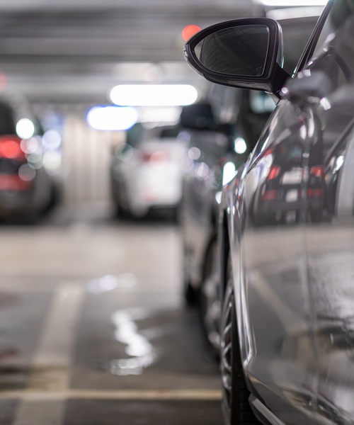 Close-up of the side mirror of a car in a blurred parking garage with cars in the background.