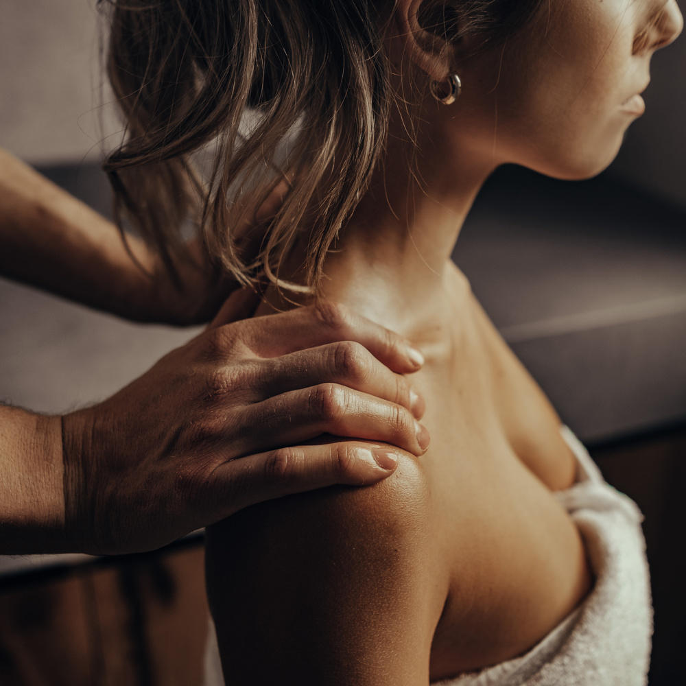 A person with a towel wrapped around their chest receives a shoulder massage from another person.